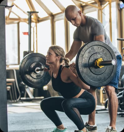 A trainer helps a woman lift heavy weights