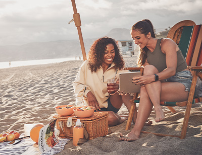 2 women sitting on beach looking at ipad