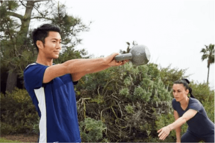 Female NASM trainer guiding male client through kettlebell swing workout