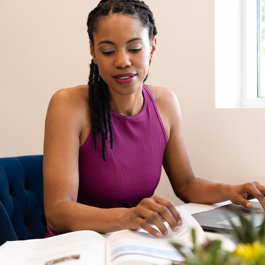 Female sitting at table with textbook and laptop in front of her