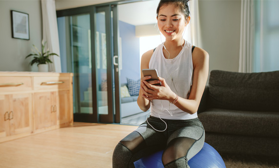 A woman using her phone on a medicine ball