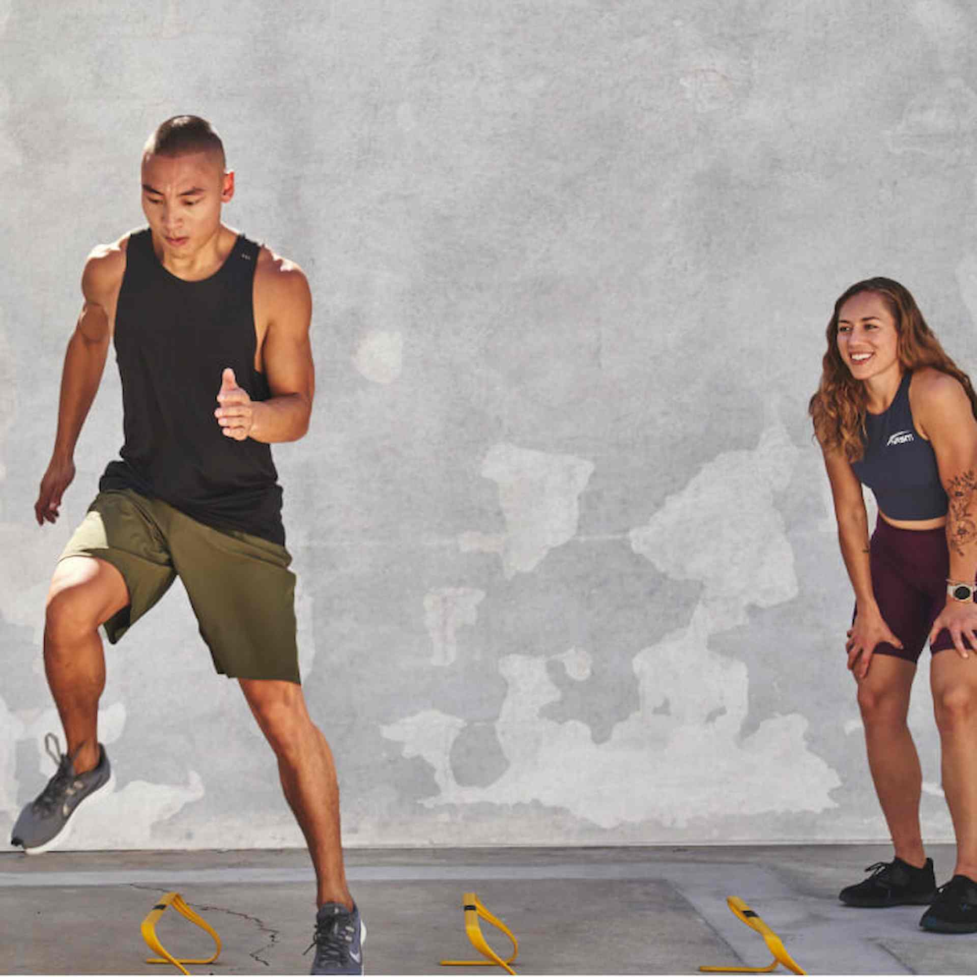 A male doing high steps while a female trainer coaches him