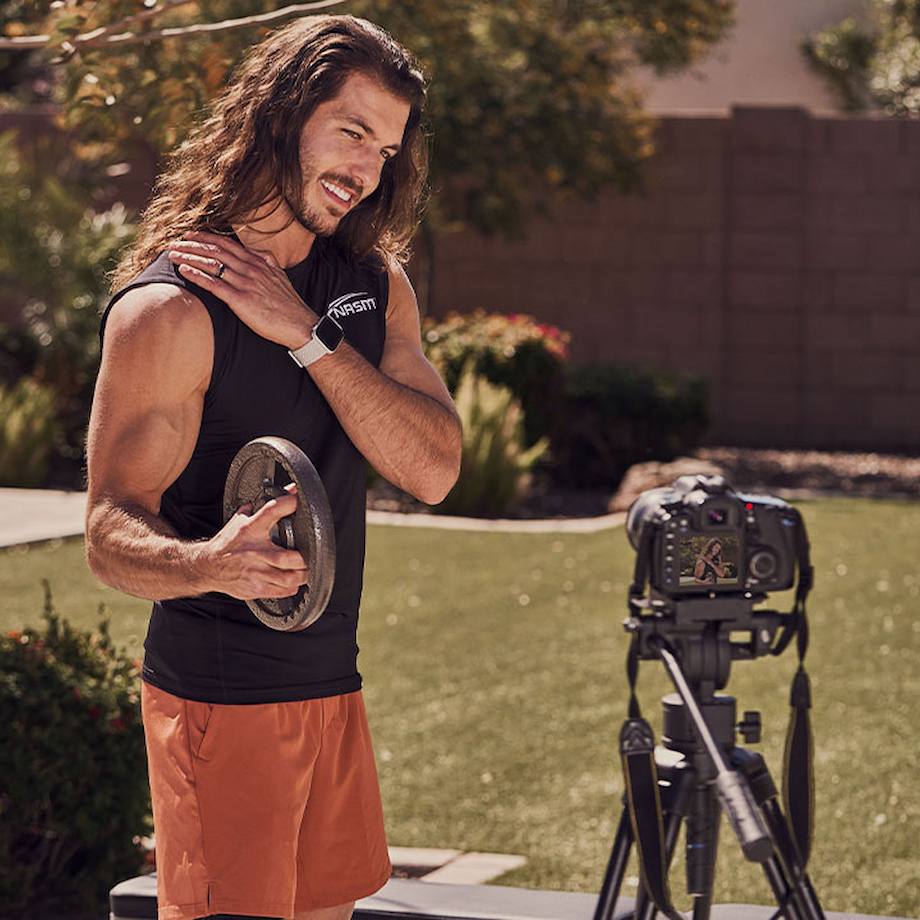 Male NASM trainer filming weighted arm workout outside