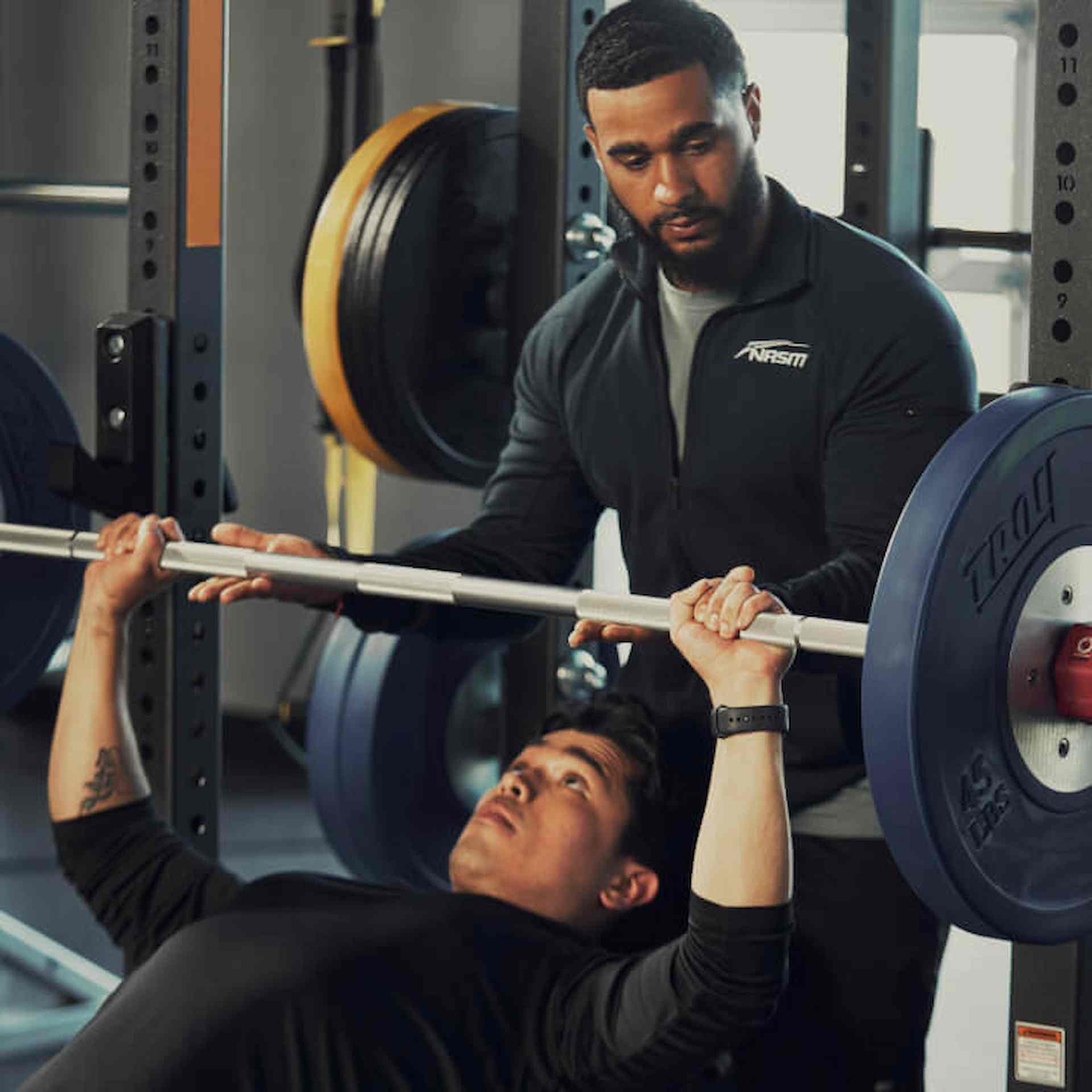 A man bench pressing with a male trainer spotting